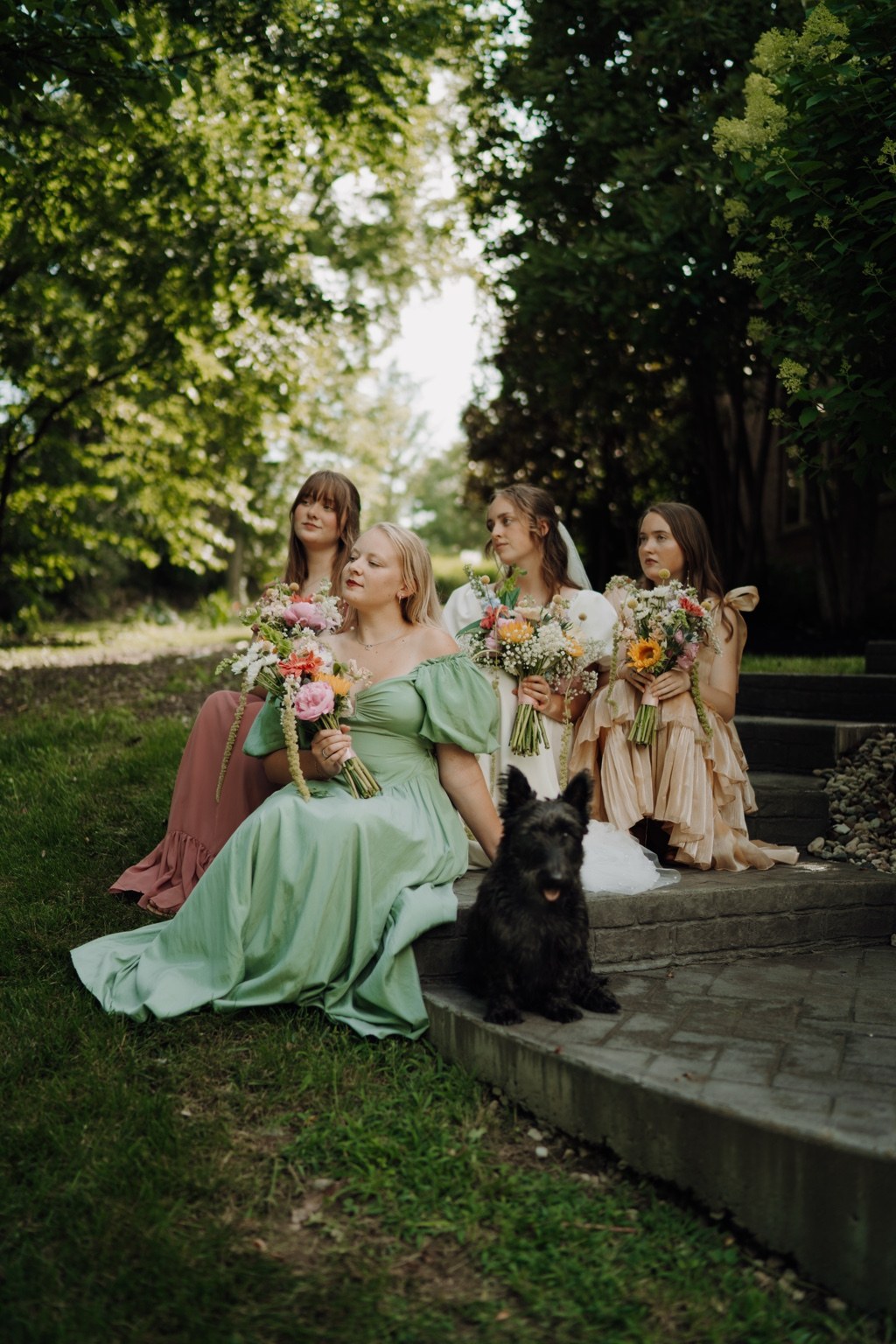 Wedding party beneath the trees with bouquets and their dog